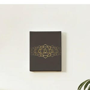 May include: A rectangular, dark brown canvas art piece with a gold-colored lotus flower and Buddha design. The artwork is mounted on a white wall, creating a minimalist aesthetic. The design is symmetrical and centered.