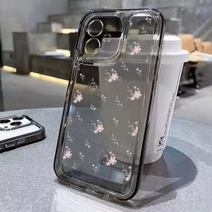 Op de afbeelding: Een transparante telefoonhoes met een bloemenpatroon. De hoes heeft een verhoogde rand rond de camera lens en een transparante achterkant.