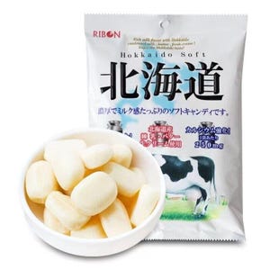 May include: A bag of Hokkaido Soft milk candy with a white background and a cartoon cow. The bag has Japanese text that says "Hokkaido" and "Hokkaido Soft". The candy is white and shaped like small, irregular ovals. The bag is open and the candy is spilling out.