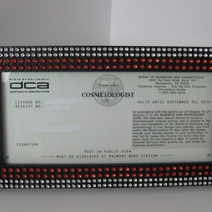 May include: A black and red framed license for a cosmetologist. The license is from the State of California Department of Consumer Affairs. The license is valid until September 30, 2014. The license is in a black frame with red and clear rhinestones.