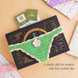 May include: A green and cream crochet book cover shaped like underwear, with a small flower accent, rests on a black book. The book has gold lettering and the text "IMMORTAL" is visible. The image includes the text "A cheeky gift for readers who love a little fun."