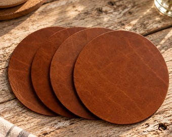 May include: A set of four circular brown leather coasters with a smooth, textured surface. The coasters are arranged in a slightly overlapping row, showcasing their consistent round shape and rich, warm tan color tone.