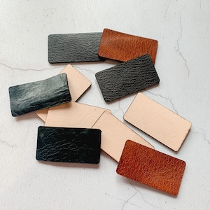 May include: Assortment of leather swatches in black, brown, and beige. The swatches are rectangular and have a textured surface.