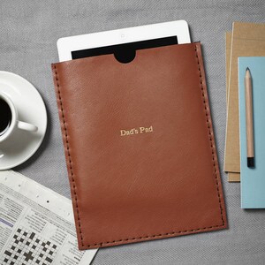 May include: A brown leather tablet case with a flap closure and a gold inscription that reads "Dad's Pad".