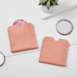 May include: Two pink leather pouches with white stitching, each designed to hold a small round mirror. One pouch has a patterned mirror inside, while the other is empty.