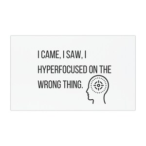 May include: A white rectangular sign with black text that reads "I CAME, I SAW, I HYPERFOCUSED ON THE WRONG THING." A black line drawing of a head with a target inside is on the right.