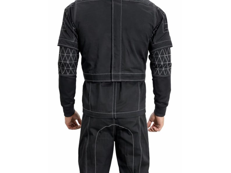 Op de afbeelding: Zwart jumpsuit met witte stiksels. De outfit heeft geometrische patronen op de mouwen en een gestructureerd ontwerp. De achteraanzicht toont het volledige kledingstuk, waarbij de getailleerde pasvorm en contrasterende stiksels worden benadrukt.