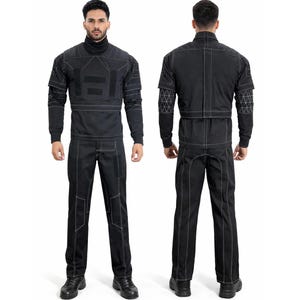 Op de afbeelding: Zwart jumpsuit met witte stiksels en geometrische accenten. De top met lange mouwen heeft een coltrui en patchdetails. De broek heeft knielappen. Het model draagt zwarte schoenen.