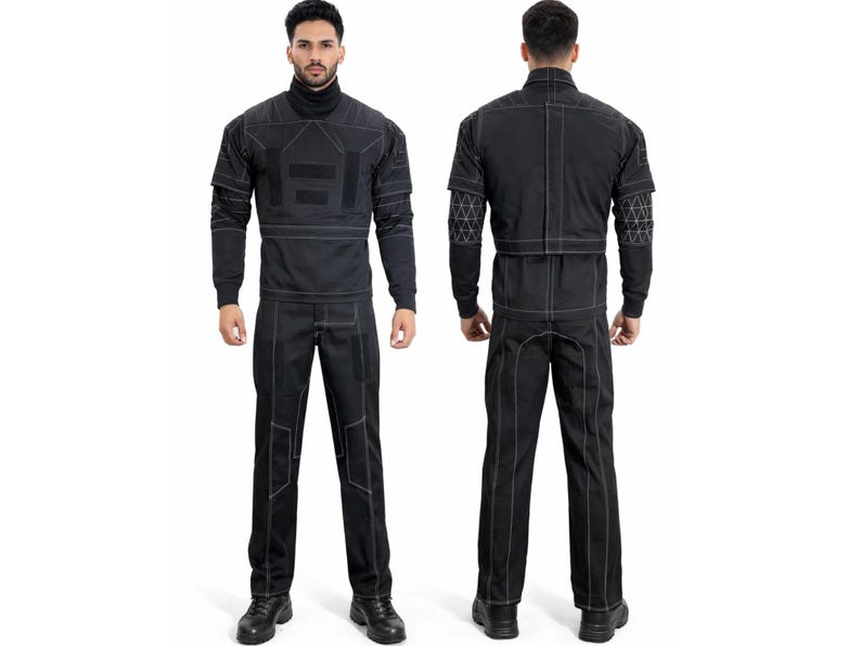 Op de afbeelding: Zwart jumpsuit met witte stiksels en geometrische accenten. De top met lange mouwen heeft een coltrui en patchdetails. De broek heeft knielappen. Het model draagt zwarte schoenen.