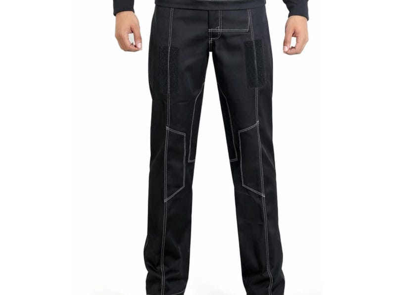 Op de afbeelding: Zwarte broek met witte stiksels en verstevigde patches. De broek heeft een recht model en is gemaakt van duurzaam materiaal. De stiksels cre&euml;ren een geometrisch patroon op de knie&euml;n en zijkanten.