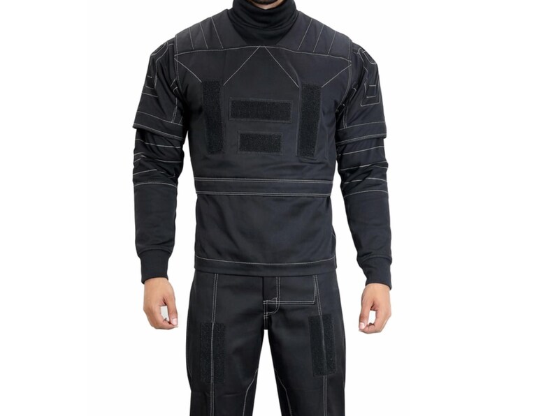 Op de afbeelding: Zwart tactisch uniform met een coltrui, lange mouwen en een bijpassende broek. Het uniform heeft witte stiksels en meerdere klittenband patches. Een functioneel en stijlvol ontwerp.