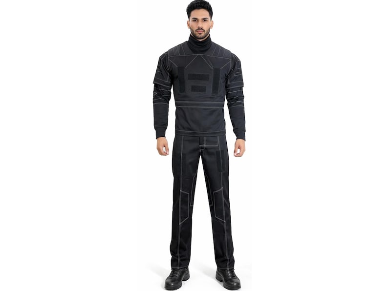 Op de afbeelding: Een zwart tweedelig outfit met witte stiksels. De top is een coltrui met lange mouwen en geometrische ontwerpen. De broek heeft rechte pijpen met bijpassende stiksels. De outfit wordt gedragen met zwarte schoenen.