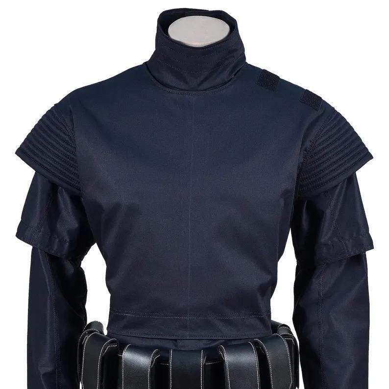 May include: A navy blue costume top with a high collar and structured shoulder details. The top features layered sleeves and a belt with multiple compartments. The costume is displayed on a mannequin.
