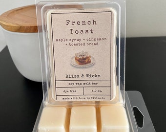 Op de afbeelding: Een drietal sojawas smelttabletten in een doorzichtige plastic verpakking. Het etiket vermeldt "French Toast" met de beschrijving "ahornsiroop + kaneel + geroosterd brood". Het merk is "Bliss & Wicks" en de smelttabletten zijn kleurvrij en 3,0 oz.