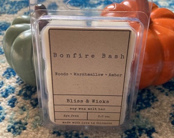 May include: A clear plastic container with a white soy wax melt bar inside. The label reads "Bonfire Bash" with the scent description "Woods + Marshmallow + Amber". The label also says "Bliss & Wicks", "Soy wax melt bar", "Dye free", "3.0 oz.", and "Made with love in Illinois".