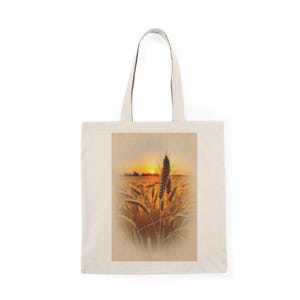 Könnte beinhalten: Eine cremefarbene Stofftasche mit einem rechteckigen Grafikdruck eines Weizenfeldes bei Sonnenuntergang. Das Bild zeigt goldene Weizenähren, die sich vor einem warm leuchtenden orangefarbenen und gelben Horizont abheben, mit weichem Rand.