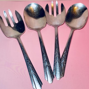 May include: Four silver serving utensils, including two spoons and two forks, are arranged on a pink surface. The utensils have long, decorative handles with a geometric design. The spoons have rounded bowls, and the forks have tines.