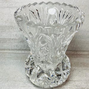 May include: A clear, cut-glass vase with a flared top and a rounded base. The vase features intricate geometric patterns and a scalloped rim. The glass reflects light, creating a sparkling effect. The vase is likely for decorative purposes.