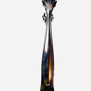 May include: A silver-toned metal drawer pull with a long, slender body and a decorative, fan-shaped top. The handle features a smooth, reflective surface with subtle curved detailing along the edges, terminating in a flat, rectangular base.