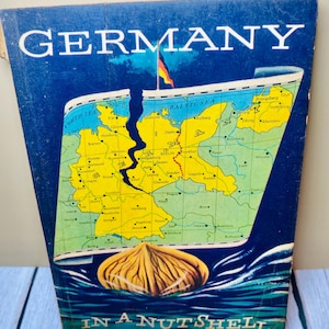 May include: Vintage travel brochure titled "GERMANY" with a map of Germany and the Baltic Sea. The brochure features a cracked map design and the phrase "IN A NUTSHELL" at the bottom, all set against a blue background.