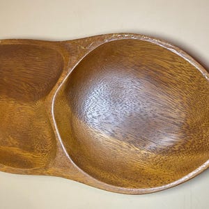 Puede incluir: Una bandeja de madera para servir con un acabado natural. La bandeja tiene dos compartimentos y un asa. La veta de la madera es visible y la bandeja es de color marrón cálido. La bandeja mide aproximadamente 46 cm de largo.