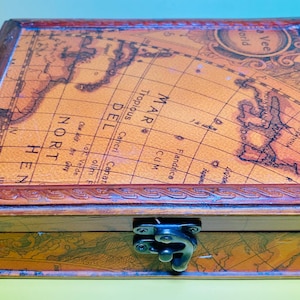 May include: A wooden box with a map design on the lid. The box has a dark brown frame and a metal clasp. The map features geographical details and text, including "Northern" and "Mar Del". The box is likely for storage or decorative purposes.