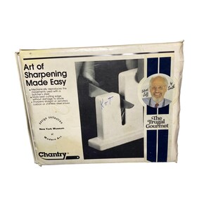 K&ouml;nnte beinhalten: Ein wei&szlig;er Karton f&uuml;r einen Chantry Messersch&auml;rfer mit dem Text Art of Sharpening Made Easy, The Frugal Gourmet und New York Museum of Modern Art. Die Verpackung zeigt eine schwarz-wei&szlig;e Grafik eines Messers, das gerade gesch&auml;rft wird.