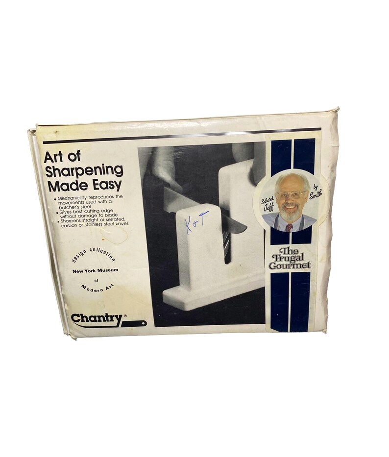 K&ouml;nnte beinhalten: Ein wei&szlig;er Karton f&uuml;r einen Chantry Messersch&auml;rfer mit dem Text Art of Sharpening Made Easy, The Frugal Gourmet und New York Museum of Modern Art. Die Verpackung zeigt eine schwarz-wei&szlig;e Grafik eines Messers, das gerade gesch&auml;rft wird.