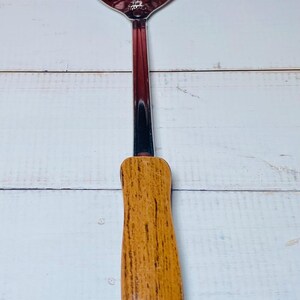 May include: A slotted spoon with a stainless steel head and a wooden handle. The spoon's head has a series of oval and teardrop-shaped holes. The handle is a light brown color.