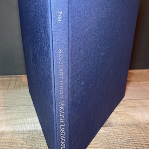 May include: A navy blue hardcover book titled "Merchant Ivory's English Landscape" with gold lettering. The book's spine features the title and author's name. The book is angled, showcasing its textured cover.