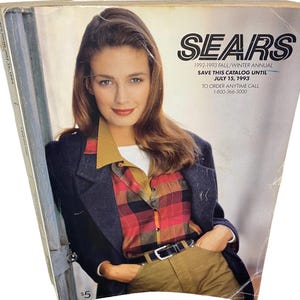 Könnte beinhalten: Ein Sears Herbst/Winter-Jahreskatalog 1992-1993 mit einer Person in einem dunklen Blazer über einem rot-schwarz-gelben karierten Hemd mit weißem Unterhemd und beigefarbener Hose. Das Cover enthält den Text SEARS, 1992-1993 FALL/WINTER ANNUAL.