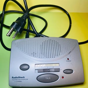 May include: A silver RadioShack FM wireless intercom with a black power cord. The intercom has buttons labeled "CALL", "TALK", and "LOCK". The text "3-CHANNEL" is also visible.