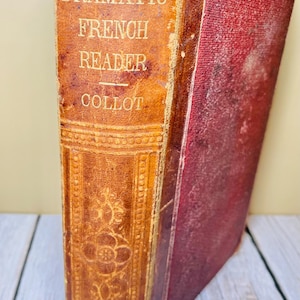 May include: An antique book titled "Dramatic French Reader" by Collot. The book has a worn, textured brown leather spine with gold lettering and decorative embossed details. The right side of the book is a faded red color.