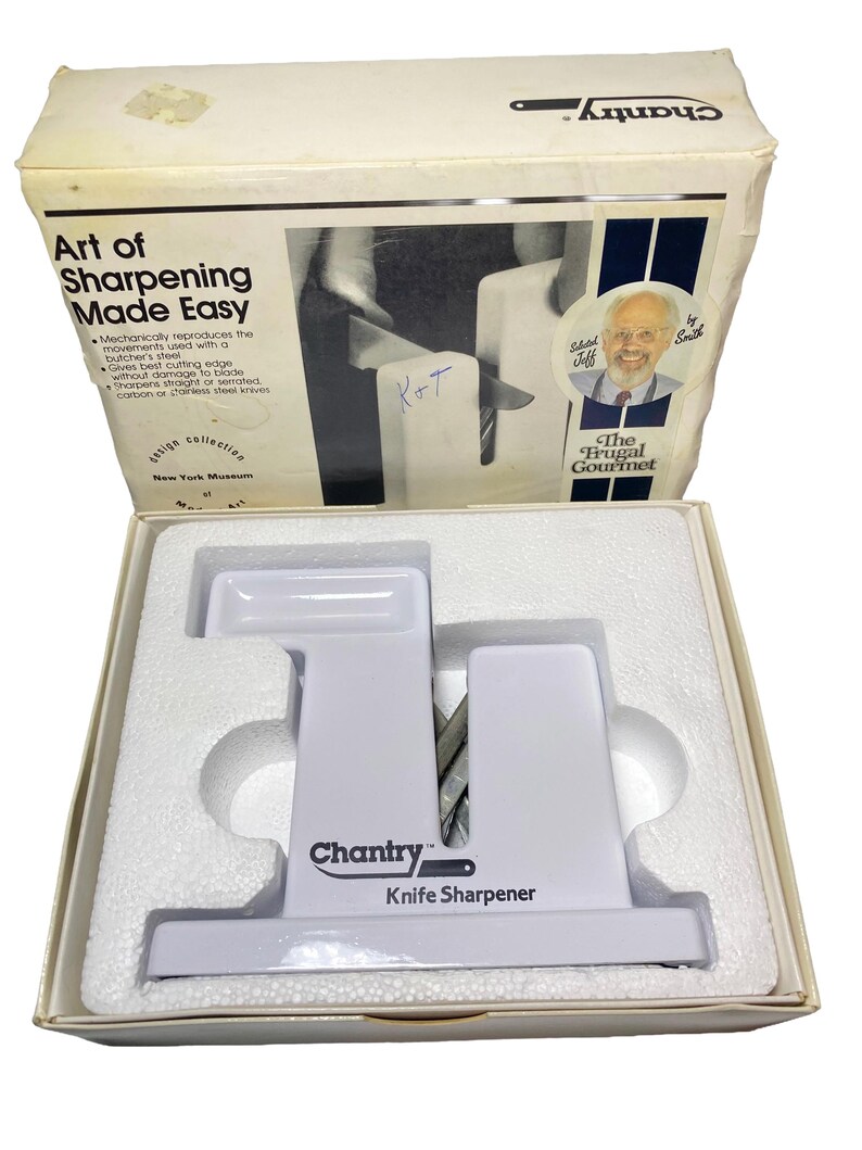 K&ouml;nnte beinhalten: Ein wei&szlig;er Chantry Messersch&auml;rfer mit V-f&ouml;rmigem Schlitz in einer wei&szlig;en Pappschachtel. Die Schachtel tr&auml;gt den Text Art of Sharpening Made Easy, The Frugal Gourmet und ein Portr&auml;t von Jeff Smith. Der Sch&auml;rfer liegt in einer wei&szlig;en Schaumstoffeinlage.