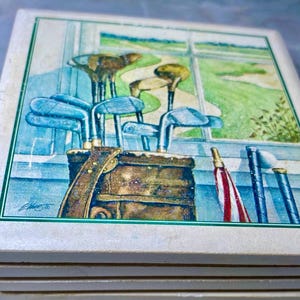 May include: A set of six square ceramic coasters with a green border. The coasters feature a watercolor painting of a golf bag with golf clubs and a window view of a golf course.