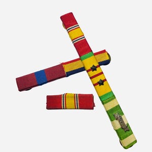 May include: Three military ribbon bars featuring various color patterns including red, yellow, blue, and green. One long vertical bar displays two black stars and a small silver metallic attachment with the number 60 engraved on its surface.