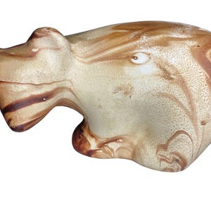 Puede incluir: Una figura de oso estilizada hecha de cerámica con un acabado suave y pulido. La superficie presenta un patrón jaspeado de tonos crema, beige y marrón oscuro, creando una apariencia fluida y orgánica en toda la forma del animal.
