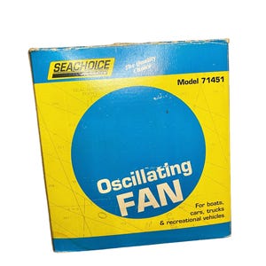 May include: A rectangular product box for a Seachoice Products oscillating fan, model 71451. The box features a bright yellow background with a large blue circle in the center, blue borders, and text stating it is for boats, cars, trucks, and vehicles.