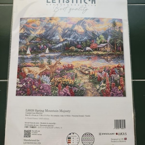 May include: A cross-stitch kit titled "Spring Mountain Majesty" by LETISTITCH. The kit features a detailed landscape scene with mountains, a lake, deer, and colorful flowers. The kit size is 17.56 x 13.19 inches and includes Aida 16 white fabric and pre-sorted threads.