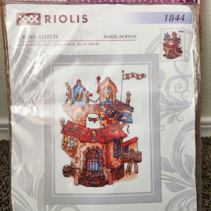 May include: A cross-stitch pattern featuring a colourful fairytale house with a red roof, blue windows, and a flag on top. The pattern is titled "Fairytale House" and is 7 inches by 9 1/2 inches.