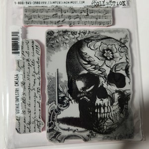 May include: A set of three clear rubber stamps featuring a black and white skull with floral details, a gothic script, and a musical score. The stamps are packaged in a clear plastic bag with the text "Stampers Anonymous" and "Jim Holtz Collection".