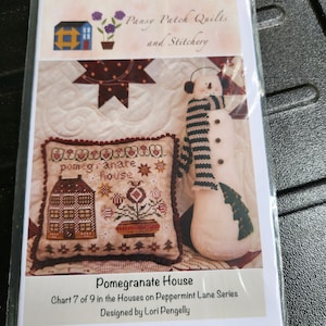 May include: A cross-stitch pattern for a house with a pomegranate design. The pattern is titled "Pomegranate House" and is chart 7 of 9 in the "Houses on Peppermint Lane" series. The pattern is designed by Lori Pengelly.