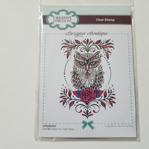 以下が含まれることがあります： 複雑なパターンと赤いバラをあしらった、精巧なフクロウのイラストが描かれたクリアスタンプ。フクロウは花柄のデザインに囲まれており、画像の下には「Owl Be There For Twit Twoo」というテキストが印刷されています。
