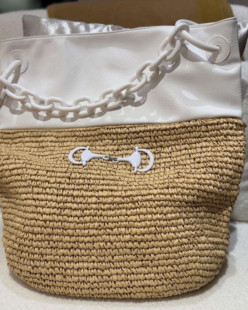 K&ouml;nnte beinhalten: Zweifarbige Tragetasche mit gewebtem Strohboden und wei&szlig;em Kunstleder-Oberteil. Die Tasche hat einen wei&szlig;en Kettenhenkel und einen dekorativen wei&szlig;en Verschluss. Die Tasche ist zum Tragen von Gegenst&auml;nden konzipiert.