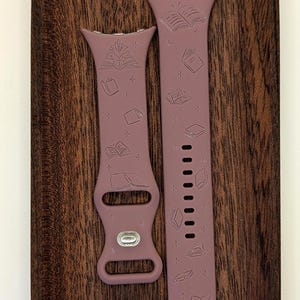 May include: Two mauve silicone watch bands with a pattern of open books and stars. The bands are designed for a smartwatch.