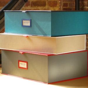 May include: Three stacked storage boxes with lids. The top box is teal blue with a black label that says "Dear Robert". The middle box is beige with a white trim. The bottom box is gray with a red trim and a label that says "Samuel Taylor Coleridge -  Hidden  Letters".