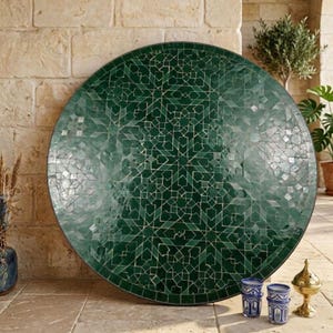 May include: A large circular table top featuring a deep green mosaic tile surface with intricate white geometric patterns. The design consists of numerous small, hand-cut tiles arranged in a complex, symmetrical star-like motif across the entire face.