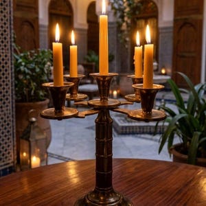 Puede incluir: Un candelabro de latón con cinco brazos que sostienen cinco velas cónicas amarillas encendidas. El soporte de metal presenta un pilar central con una base circular y portavelas escalonados. Las velas arden con llamas visibles.
