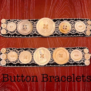 May include: Two button bracelets with a black base and white lace trim. The bracelets feature various sizes of white and iridescent buttons. The text "Button Bracelets" is at the bottom of the image.