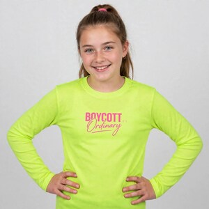 May include: A neon yellow long-sleeve shirt featuring the text BOYCOTT Ordinary printed in pink on the chest. The shirt has a crew neckline and long sleeves, providing a bright and vibrant appearance with clear, bold lettering across the front.